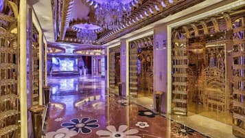 A luxurious hallway with ornate gold decorations, a reflective floor, and a grand chandelier.