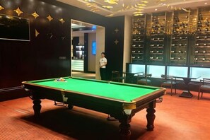 Une table de billard dans une pièce dont un mur est peint dans une couleur sombre et qui contient une étagère sur laquelle sont posés divers objets.