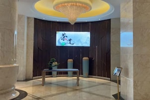 Un hall con una pantalla grande mostrando caracteres chinos, un banco y una araña.