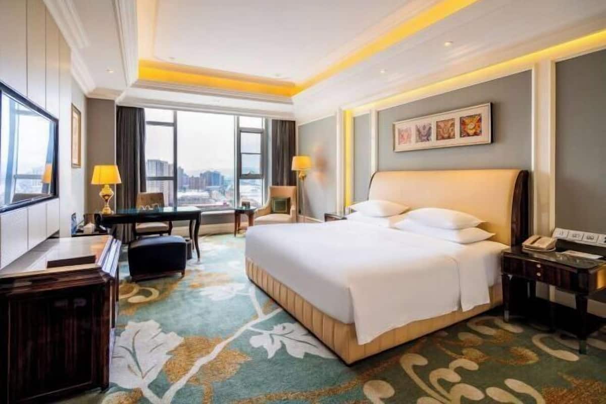 Habitación de hotel con una cama grande, un escritorio, una silla y vistas a la ciudad.