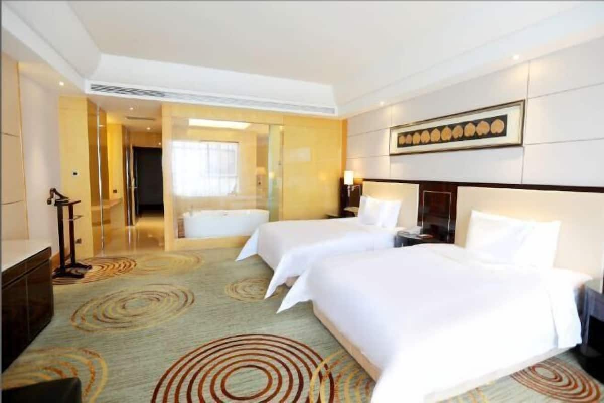 Habitación de hotel con dos camas, zona de estar, bañera y un espejo grande.