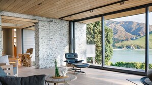 Ein modernes Interieur mit Steinwand, Blick auf einen See und Berge sowie einer Sitzecke mit Stuhl und Tisch.