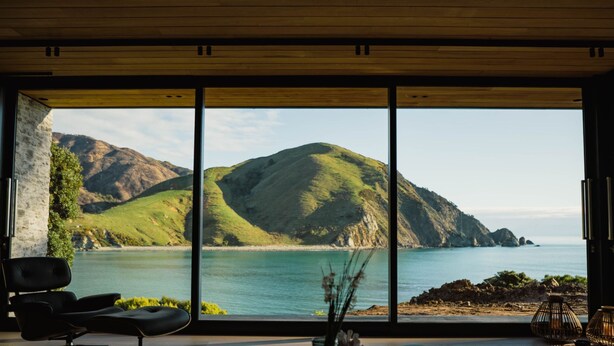 Ein modernes Interieur mit einem großen Fenster, das einen malerischen Blick auf eine gebirgige Küstenlandschaft und ein Gewässer bietet.