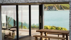 Eine Holzterrasse mit Tisch und Bänken, mit Blick auf ein Gewässer und viel Grün.