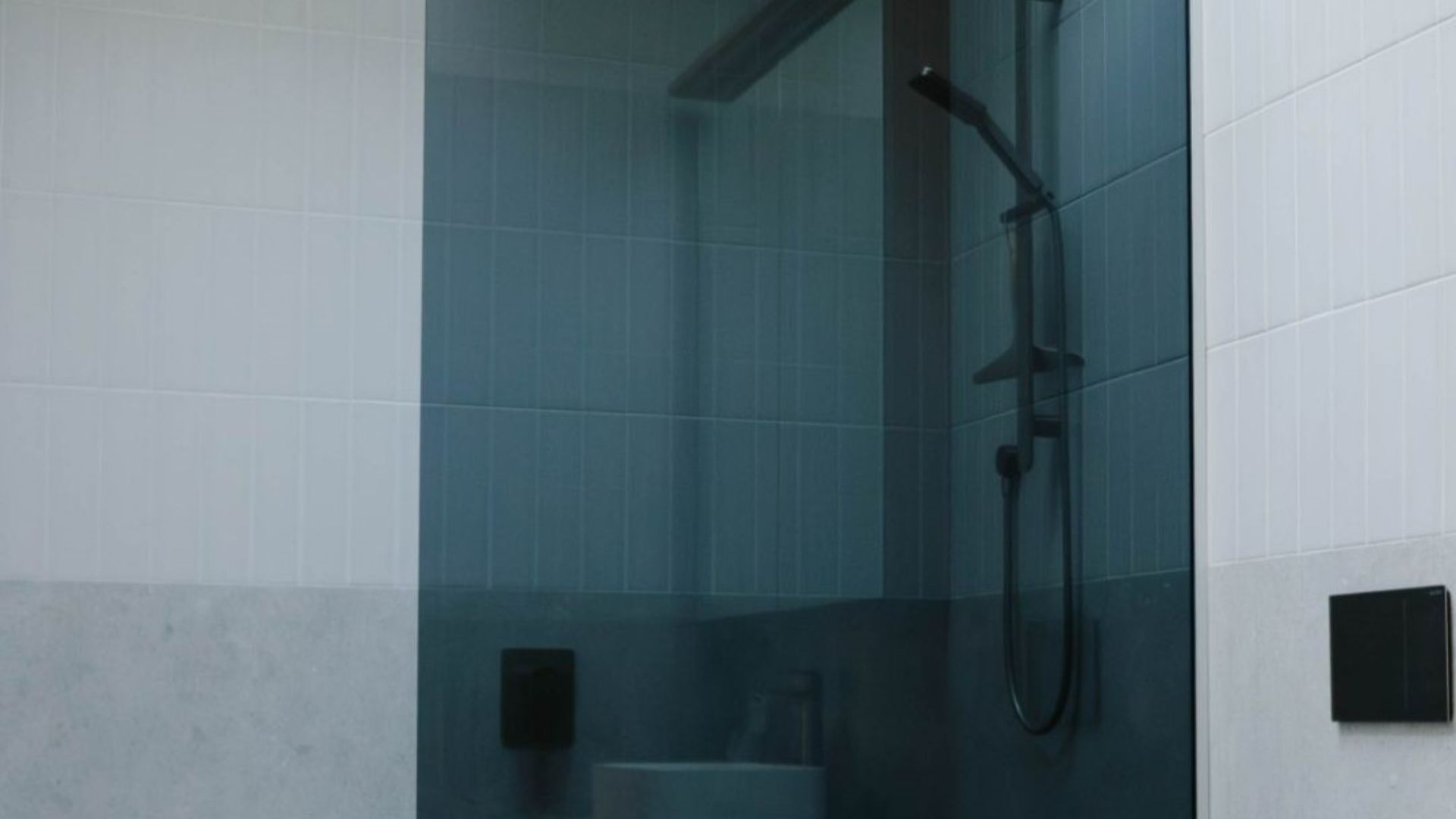Een badkamer met een glazen douchecabine, witte betegelde wanden en een zwarte handdouche.