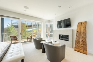 A modern living room with a sofa, armchairs, a flat-screen TV, a fireplace, and a balcony with a view of the city. - Apex Dream House Ski in/ Ski Out (Park City)