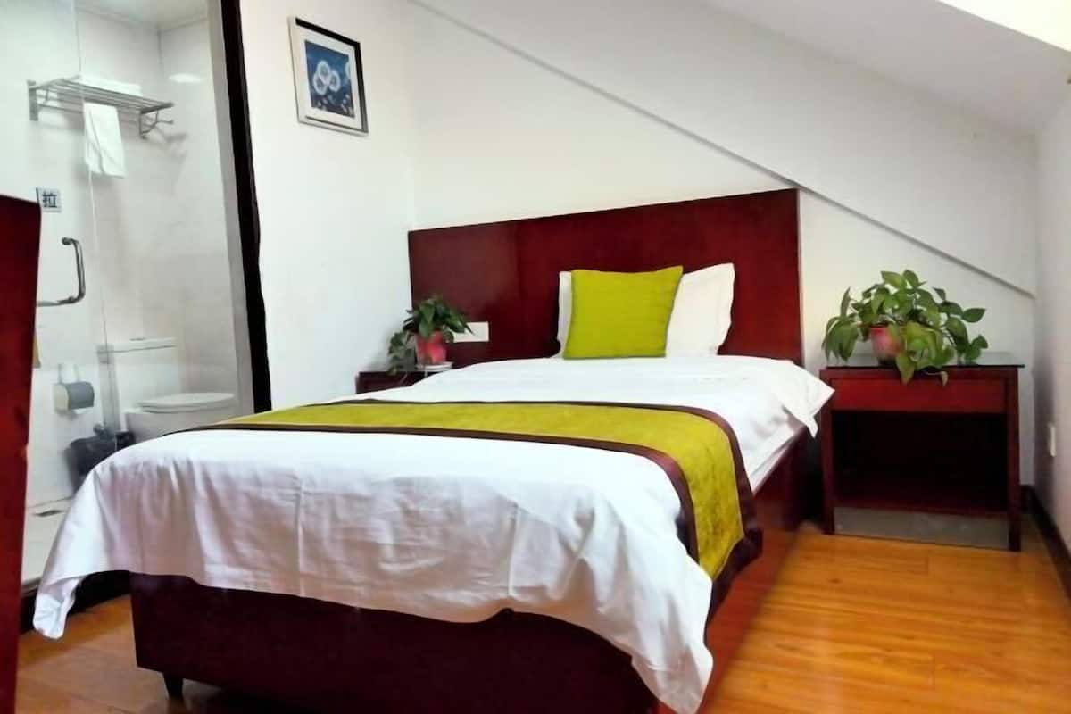 Habitación de hotel con cama, mesita de noche con planta, ducha e imagen en el marco en la pared.