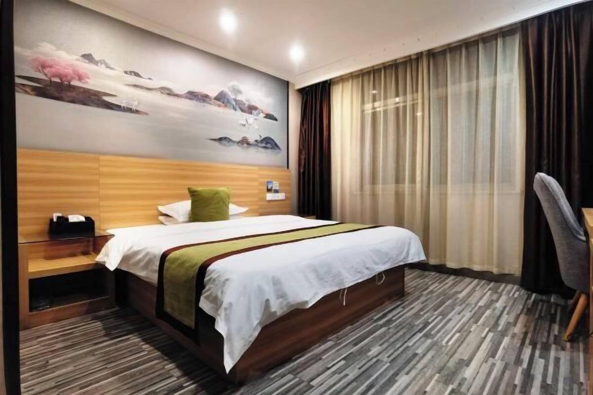 Habitación de hotel con cama, mesita de noche, escritorio, silla, un cuadro en la pared y una ventana con cortinas.