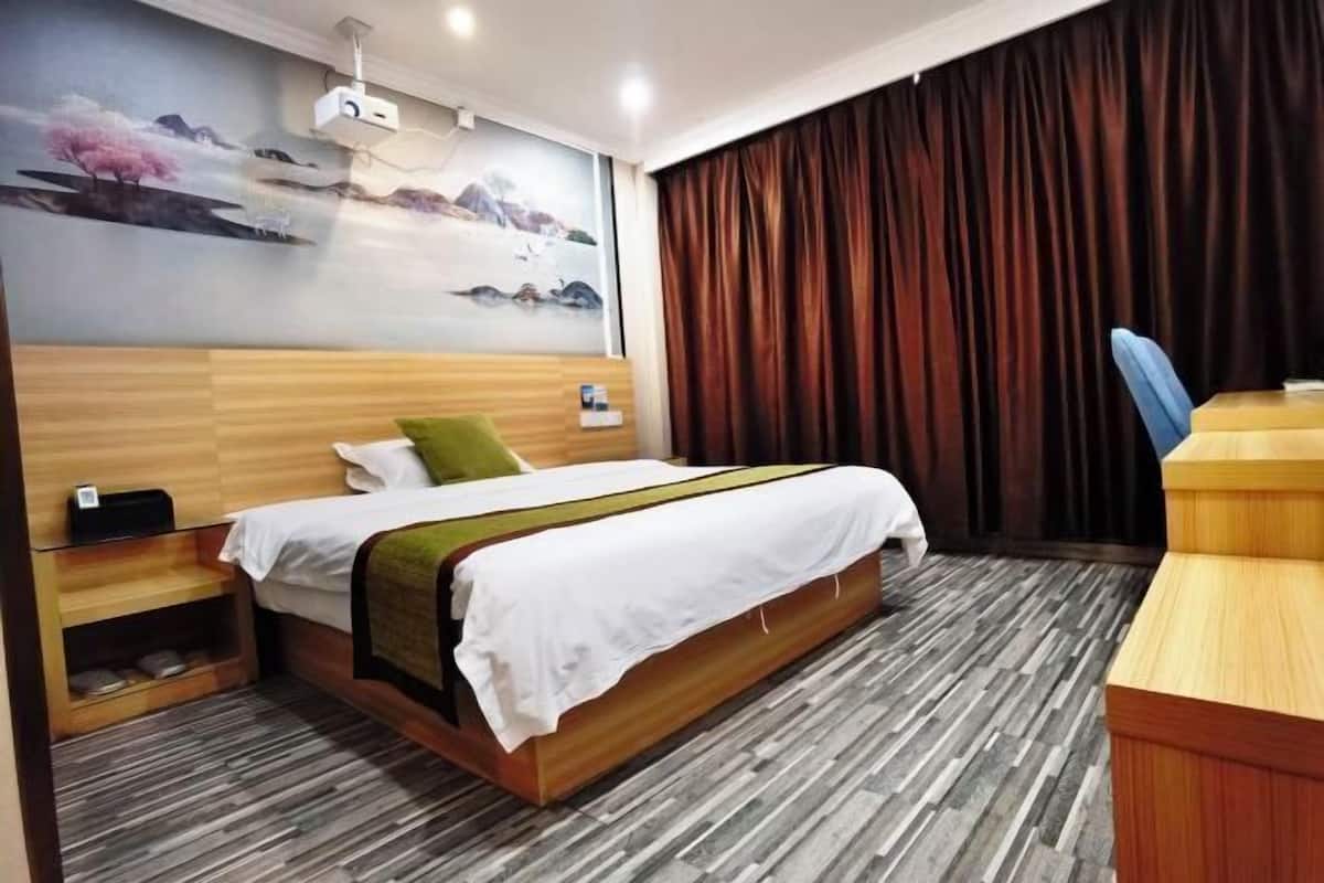 Una habitación de hotel con cama, escritorio, silla, proyector y un mural en la pared.