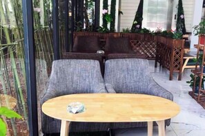 Et siddeområde med en polstret sofa og et træbord, omgivet af planter og et bambushegn.
