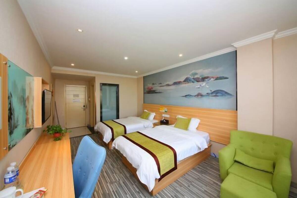Habitación de hotel con dos camas, un escritorio, una silla verde y un cuadro en la pared.