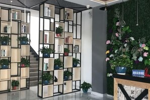 Un interior moderno con una estantería modular repleta de libros y plantas en macetas, una escalera y un panel decorativo con fondo verde.
