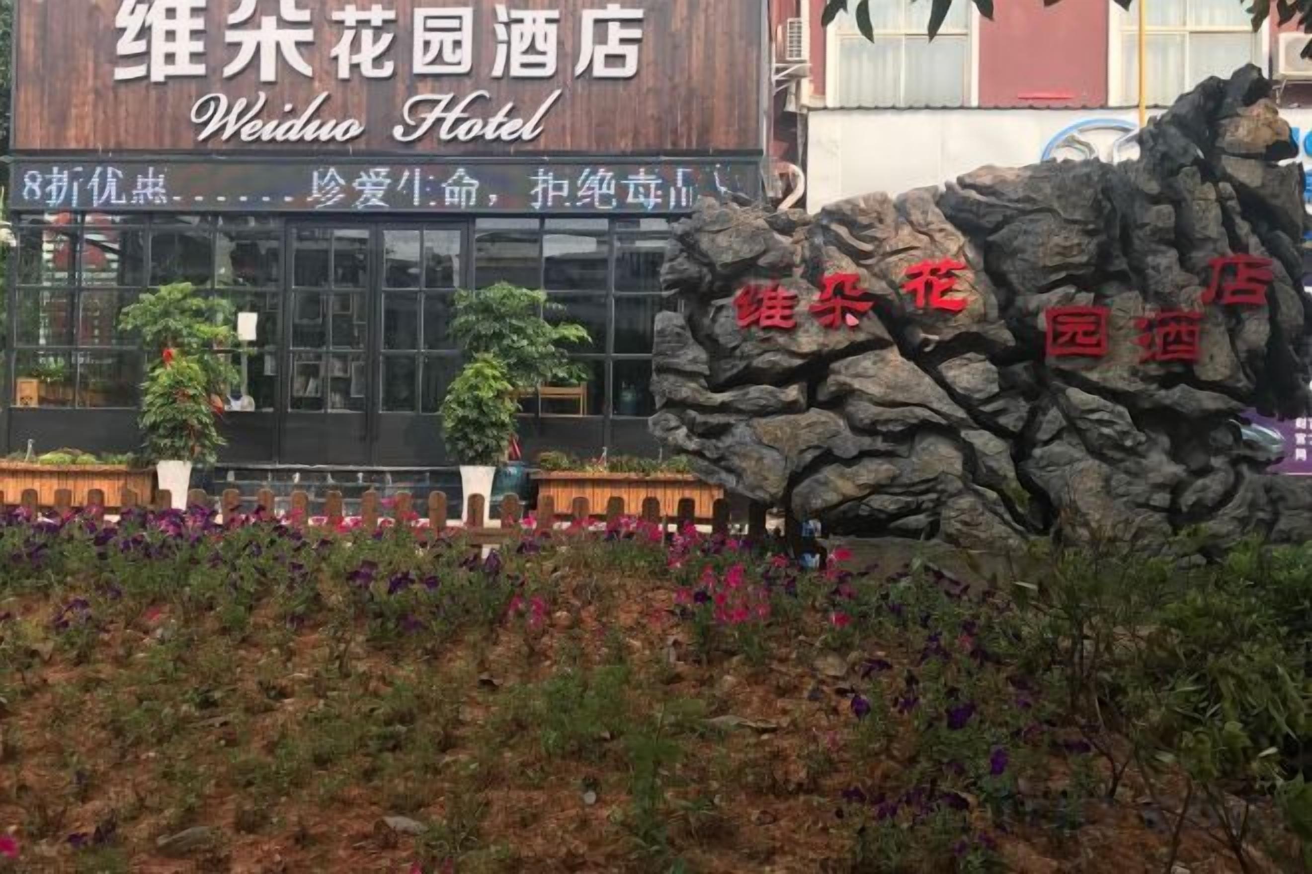Ein Hotel Schild mit chinesischen Schriftzeichen, eine große Felsformation und eine gepflegte Gartenanlage.