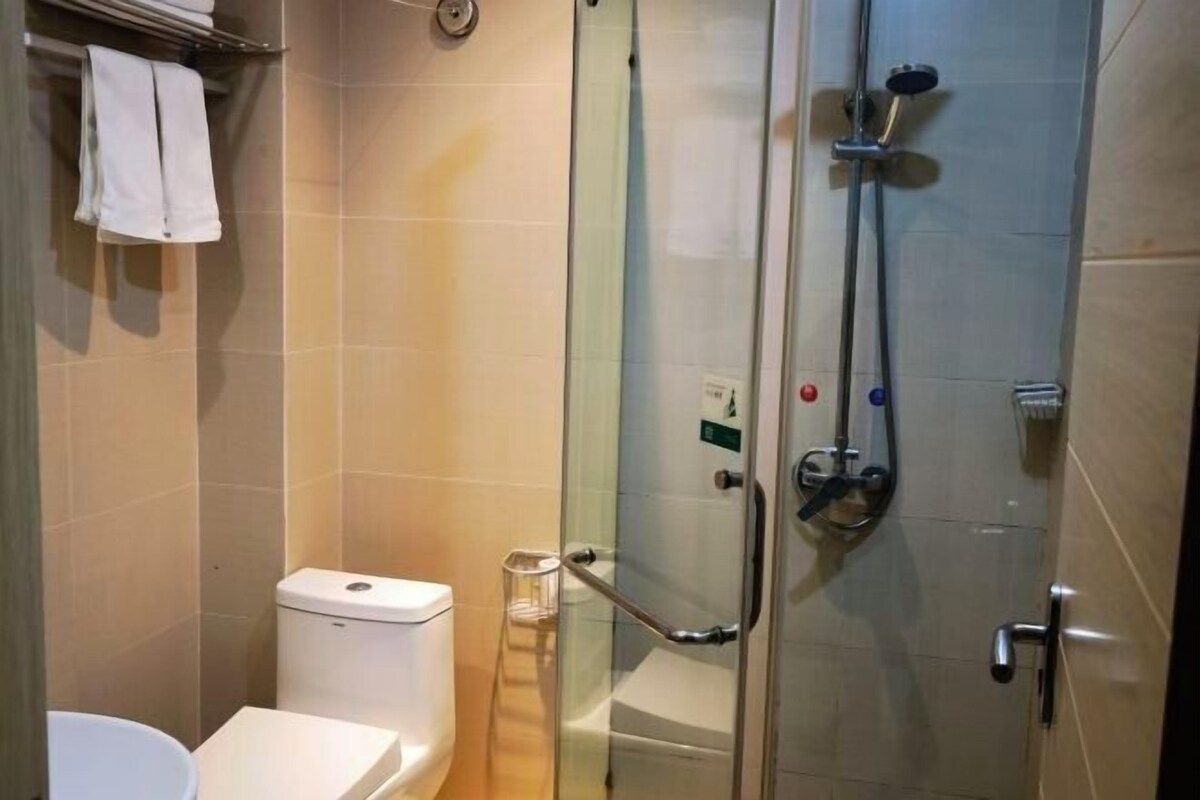 Een glazen douchecabine met een handdouche, een toilet en een handdoekrek met handdoeken.