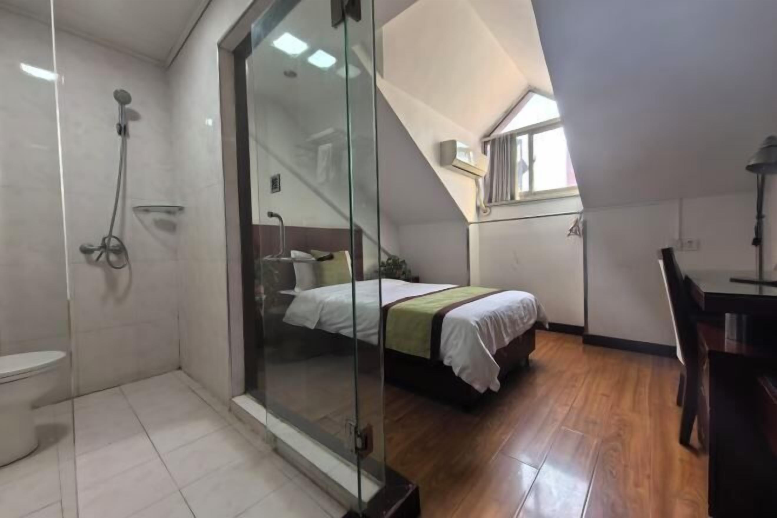 A bedroom with a glass shower enclosure, a bed, and a wooden floor.