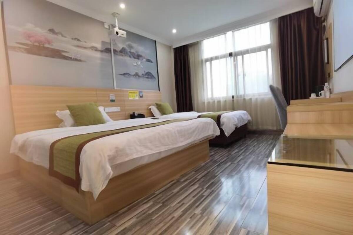 Habitación de hotel con dos camas, cabecero de madera, escritorio y un ventanal con cortinas.
