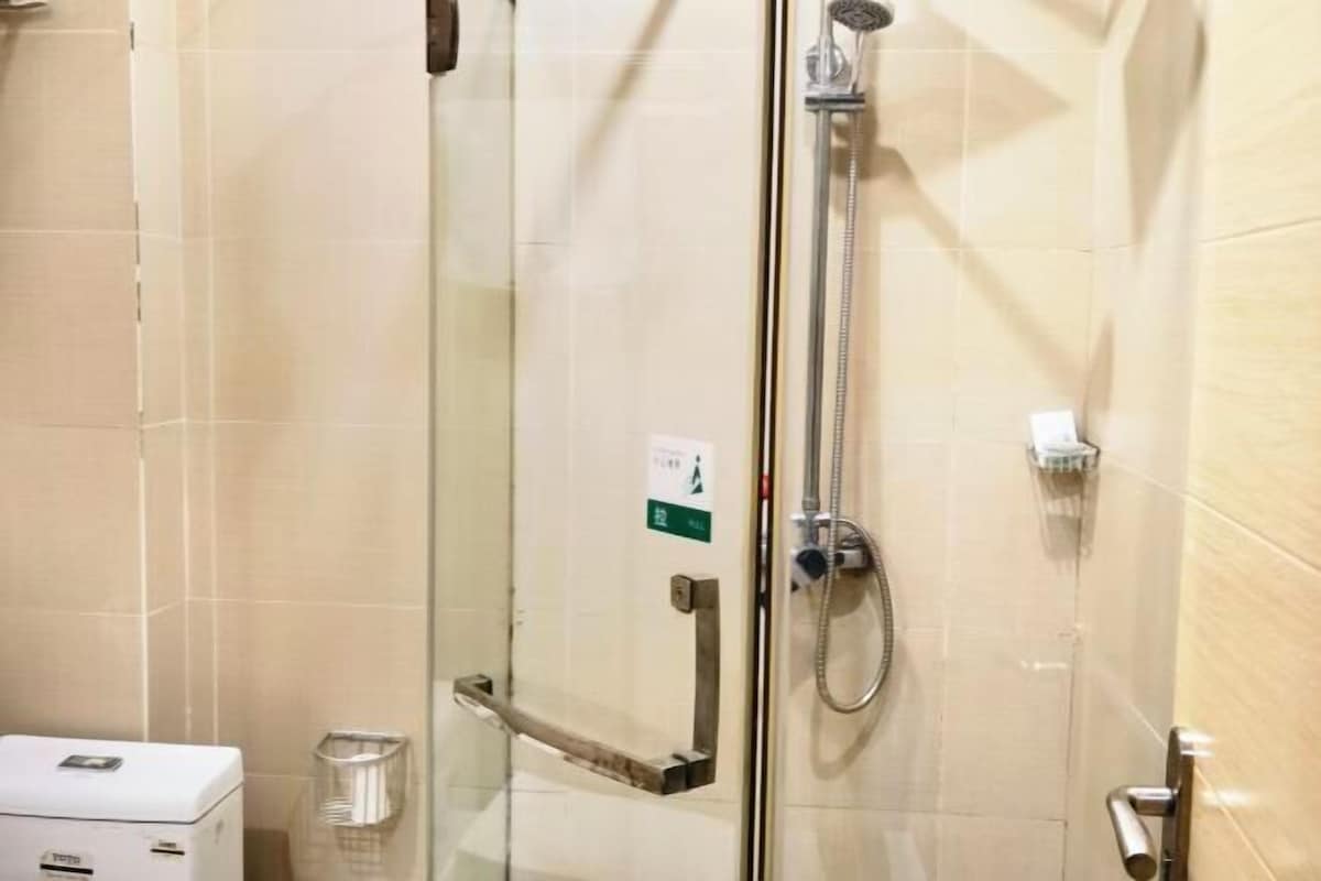 Een douchecabine met glazen wanden, een handdouche, een handdoekhouder en een prullenbak.
