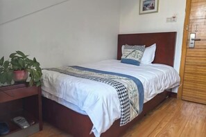 Ein Schlafzimmer mit einem hölzernen Bett, weißer Bettwäsche, einer gemusterten Tagesdecke und einem Blumentopf auf einem Nachttisch.