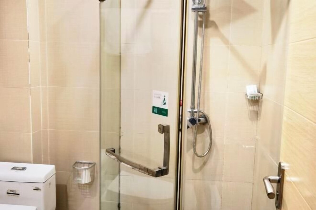 Douchecabine van glas met een handdouche, een handdoekhouder en een kleine afvalbak.