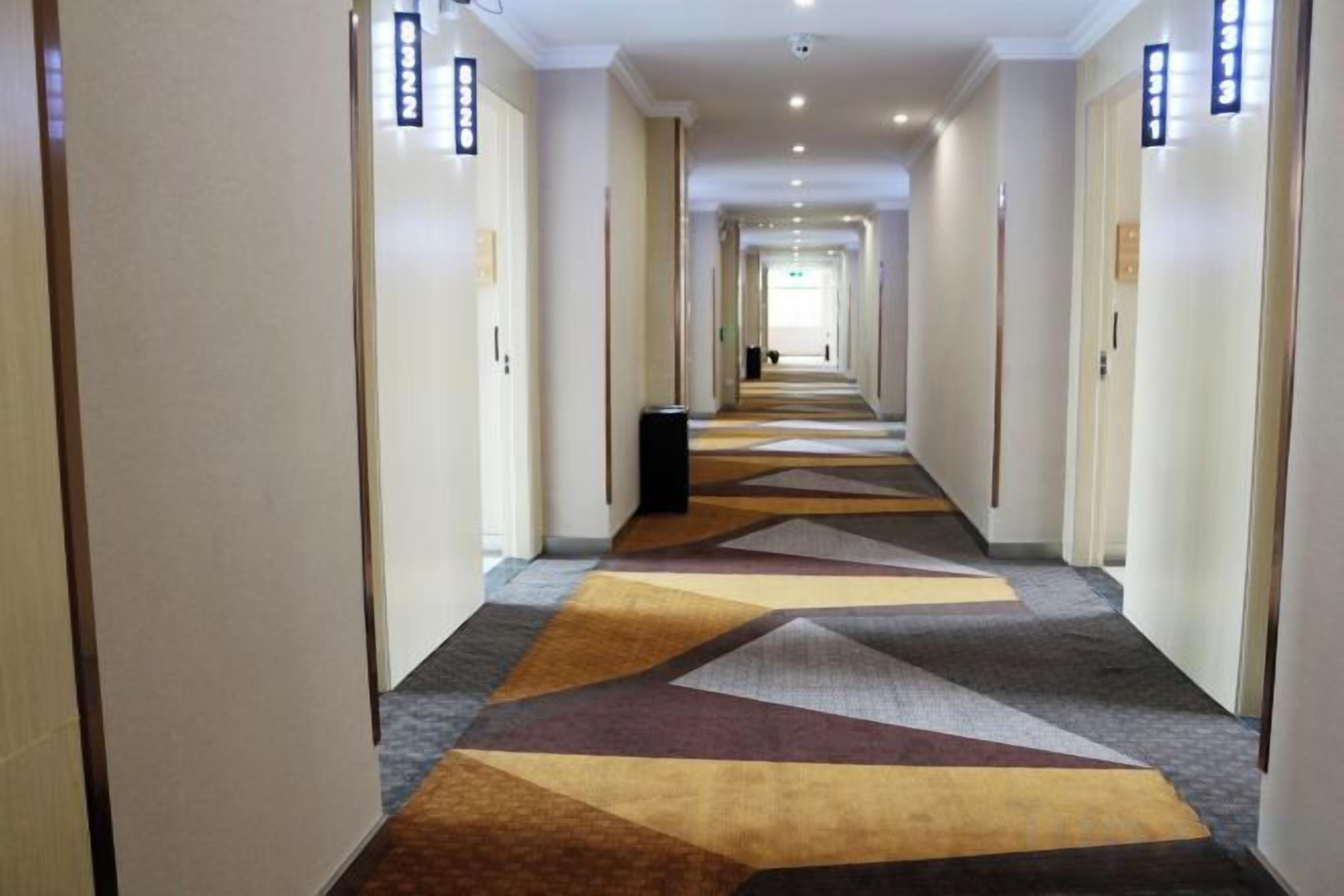 A hotel hallway with carpeted floors, doors on both sides, and a trash bin in the center.