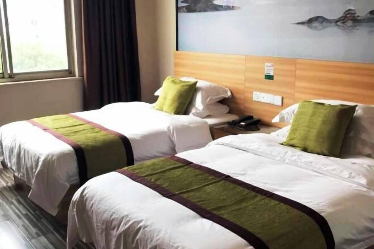 Habitación de hotel con dos camas, cabecero de madera, una ventana y una obra de arte colgada en la pared.