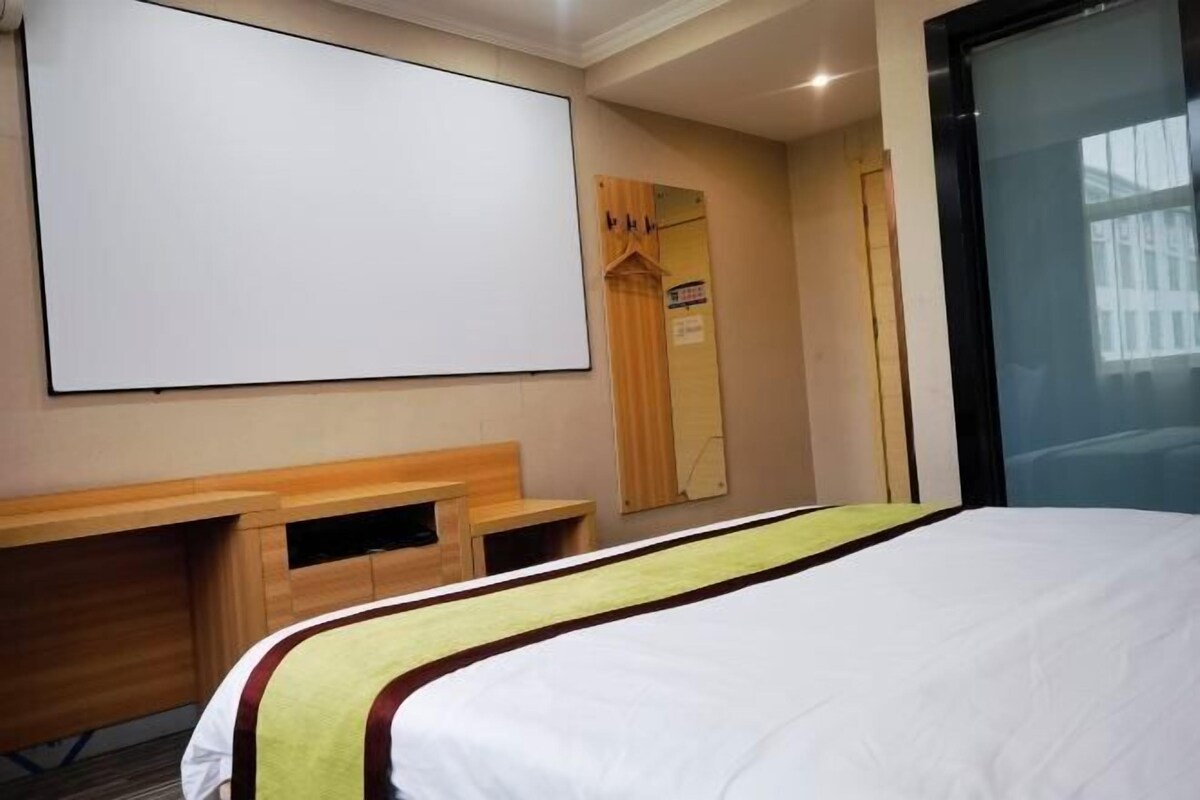 Een hotelkamer met een bed, een bureau, een spiegel en een projectiescherm.