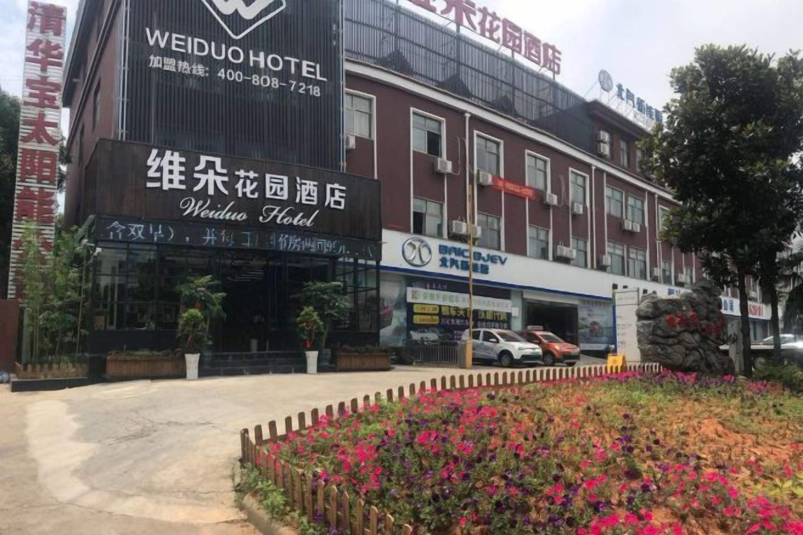 Een hotel met een opvallend bord, een parkeerplaats en een bloembed in de voortuin.