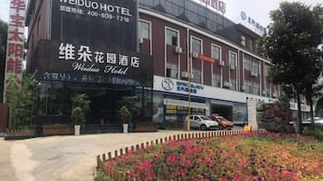 Een hotel met een opvallend bord, een parkeerplaats en een bloembed in de voortuin.
