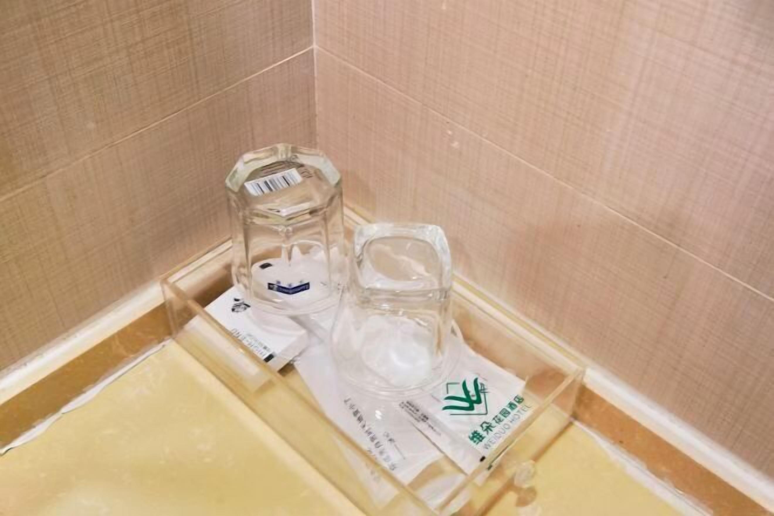 Casa de banho com parede revestida a azulejos bege, cabine de duche em vidro e lavatório branco.