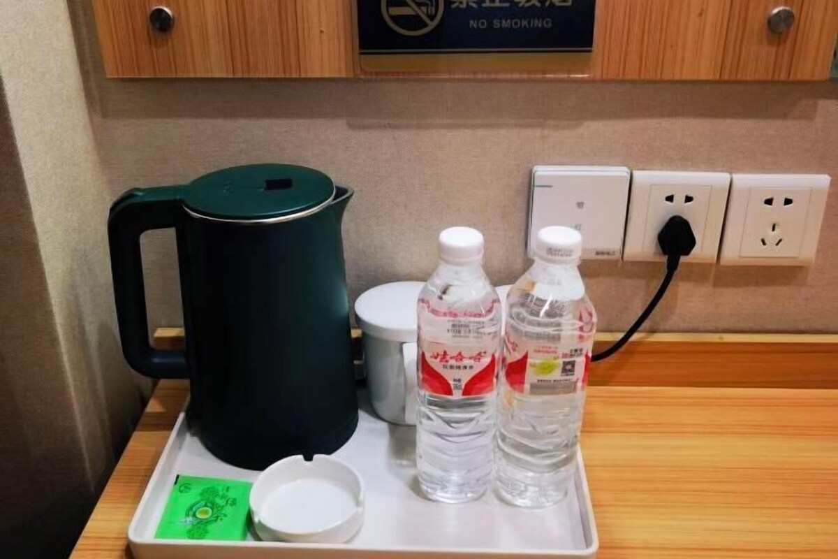 Een dienblad met een zwarte elektrische waterkoker, twee waterflesjes, een witte kop en een groene kaart op een houten tafel.