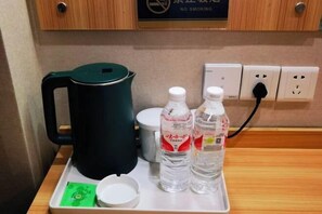 Een dienblad met een zwarte elektrische waterkoker, twee waterflesjes, een witte kop en een groene kaart op een houten tafel.