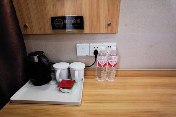 A kitchenette with a coffee maker, two white mugs, a red packet, and two bottles of water on a tray. - Tongling Weiduo Garden Hotel (Tongling)