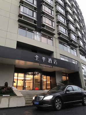 A hotel entrance with a modern facade, a car parked in front, and a sign indicating the hotel name. - Ji Hotel (Shanghai)
