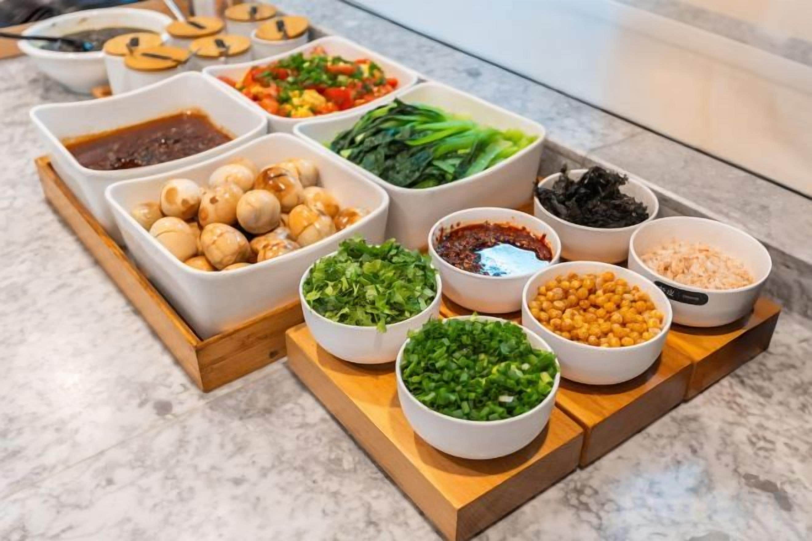A variety of food items arranged on a wooden board, including bowls of vegetables, nuts, and sauces.