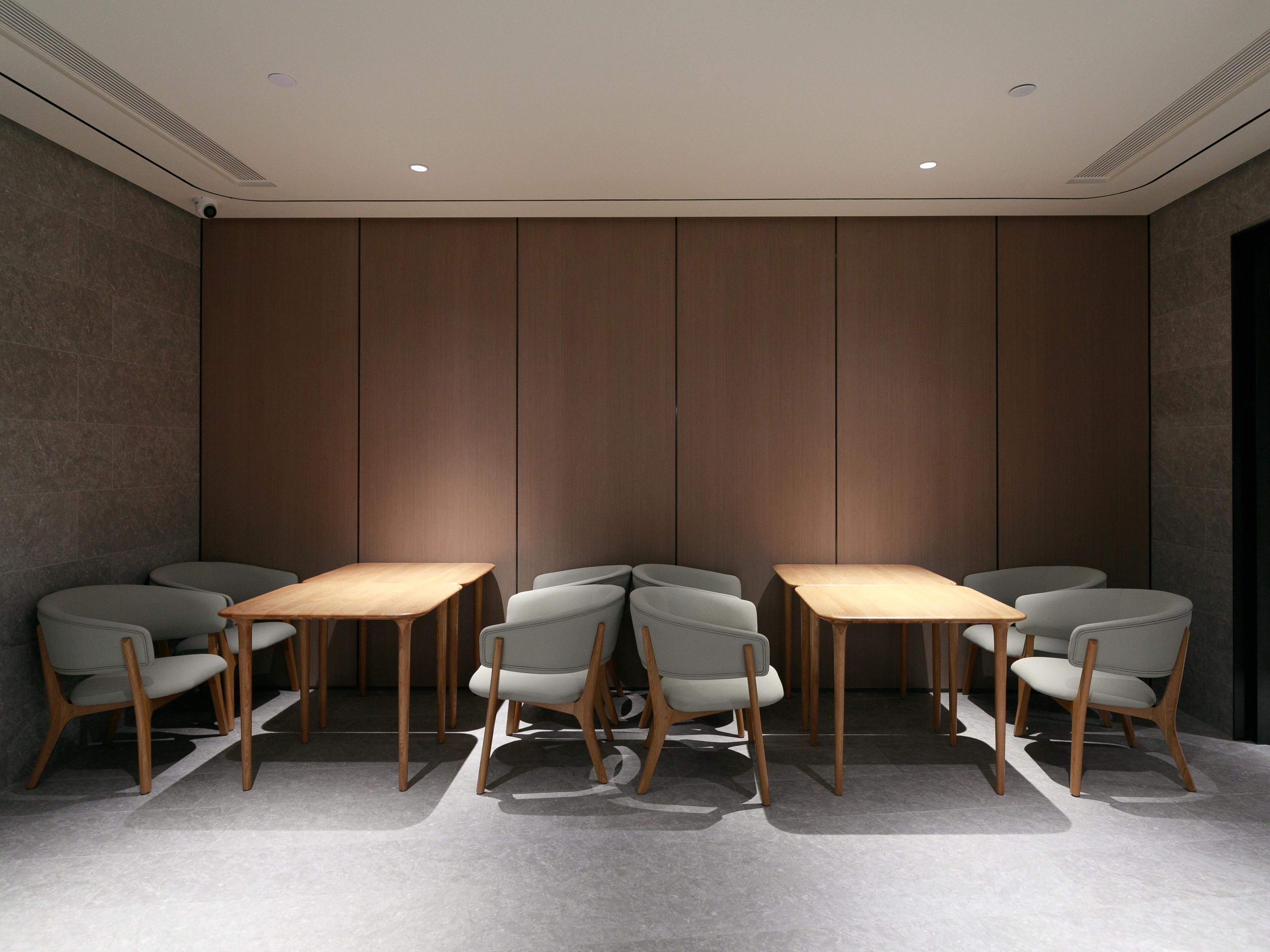 Uma sala de conferências com design moderno, com uma mesa comprida e seis cadeiras, parede de painéis de madeira e luminárias embutidas no teto.