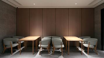 Uma sala de conferências com design moderno, com uma mesa comprida e seis cadeiras, parede de painéis de madeira e luminárias embutidas no teto.