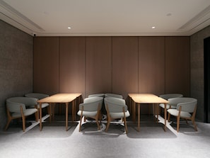 Une salle de conférence au design moderne, dotée d’une longue table et de six chaises, avec un mur en panneaux de bois et des spots encastrés au plafond.