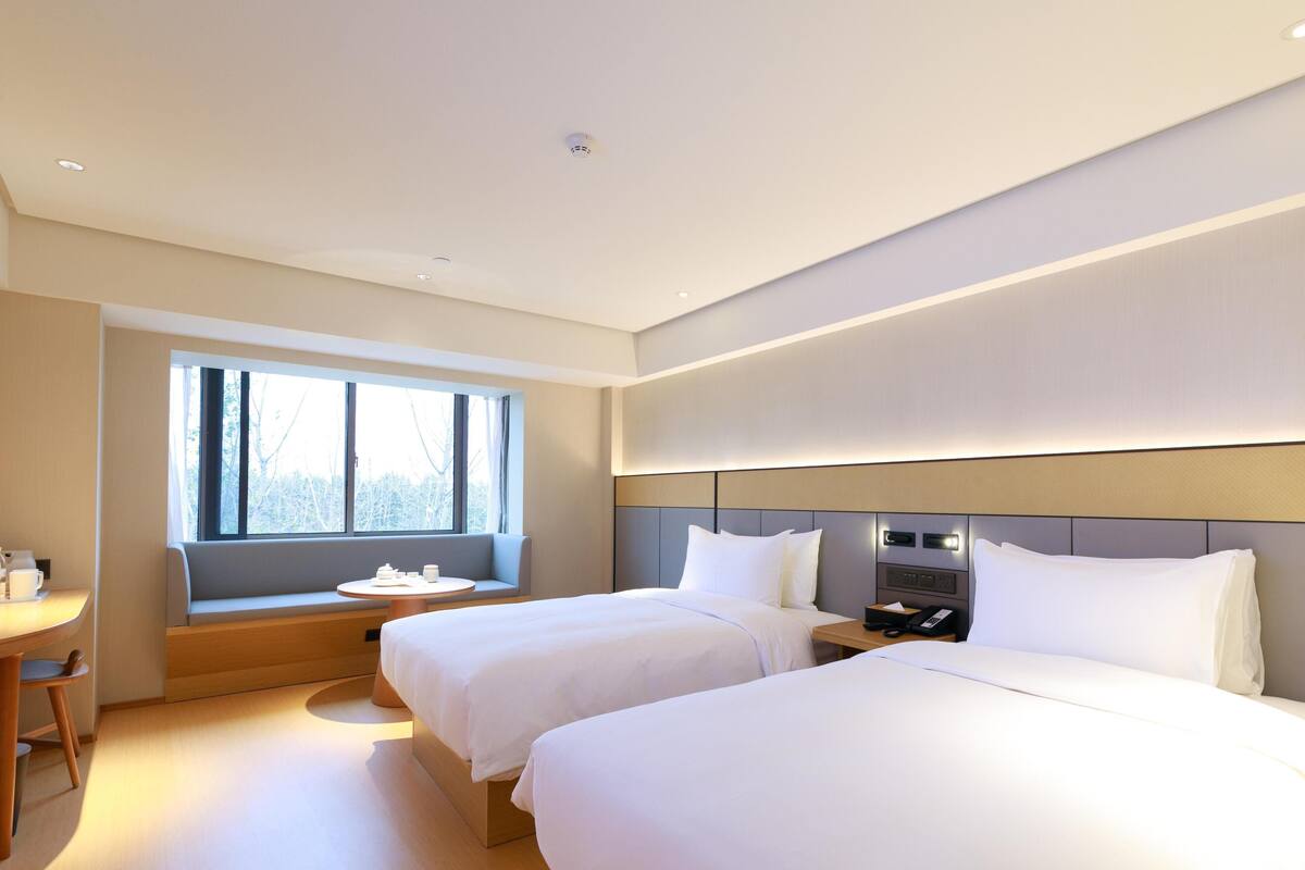 A hotel room with two beds, a seating area with a table, and a large window.