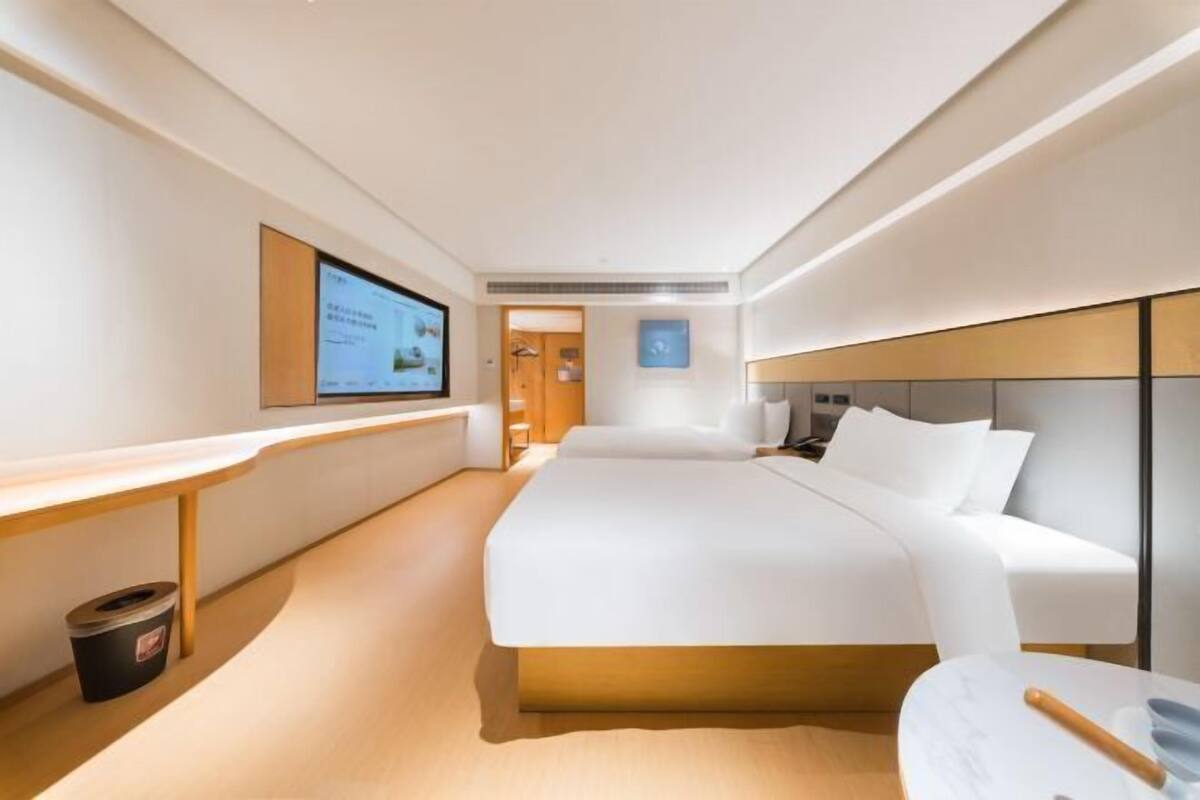 A modern hotel room with a large bed, a desk, and a television on the wall.