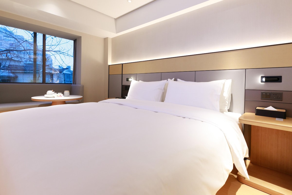 Une chambre d’hôtel moderne, dotée d’un grand lit, de tables de chevet, d’une fenêtre offrant une vue agréable et d’un panneau de commande mural.