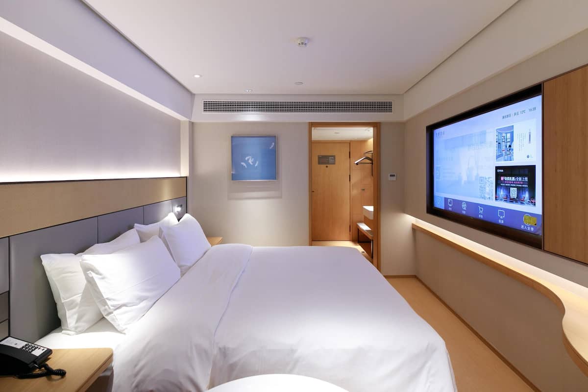 A hotel room with a bed, a TV, a phone, and a door leading to a bathroom.