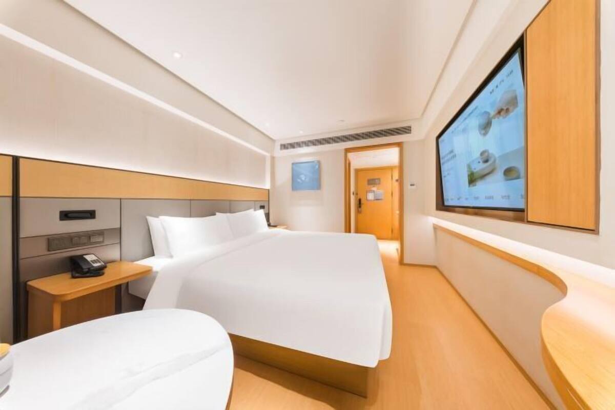 A hotel room with a bed, bedside tables, a TV, and a wooden floor.