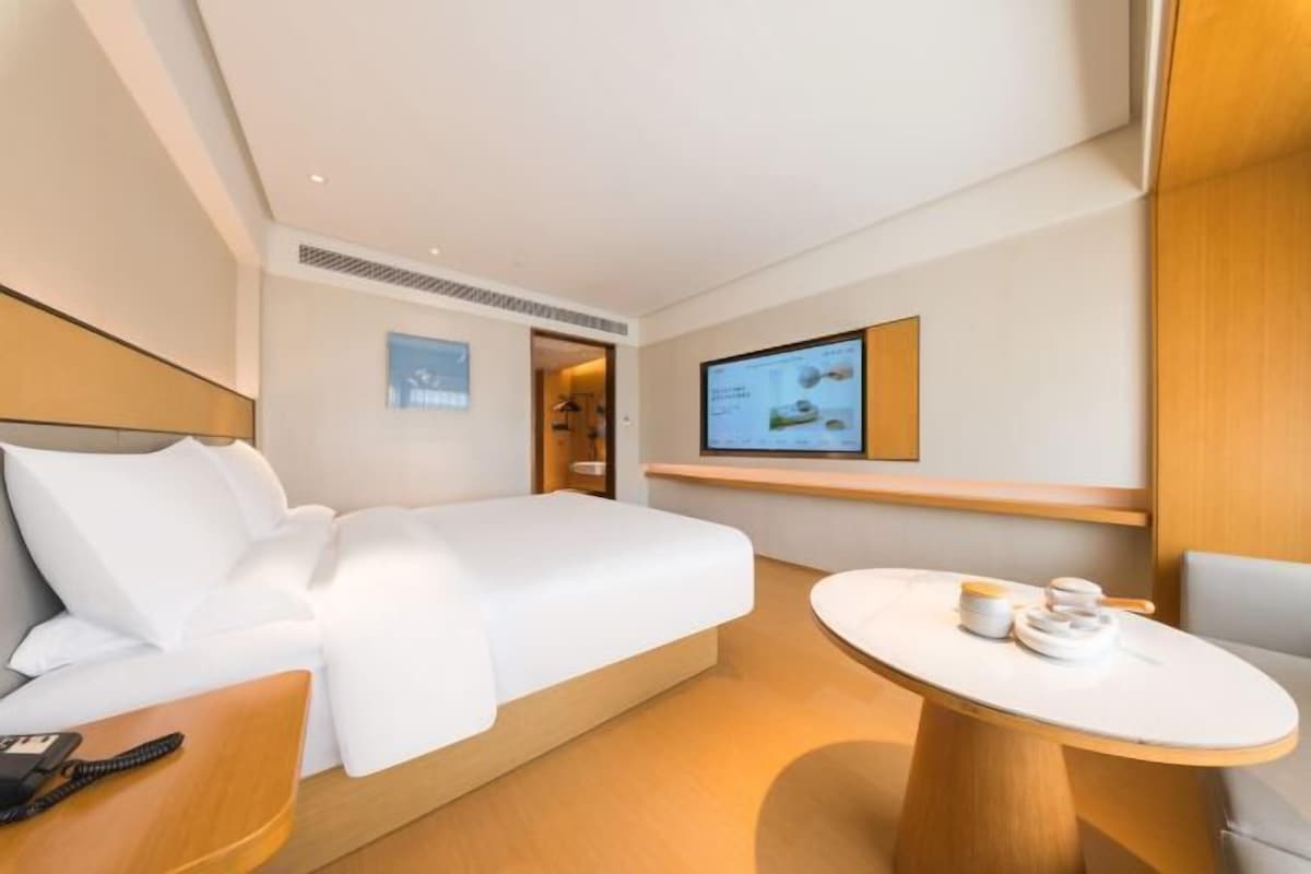 Ein Hotelzimmer mit einem Bett, einem Schreibtisch mit Telefon, einem kleinen Tisch mit Tassen sowie einem Fernseher an der Wand und einer Tür zu einem Badezimmer.