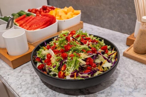 A bowl of salad with various vegetables and a tray of sliced fruits and vegetables in the background. - JI Hotel (Shanghai Pusan Road Subway Station Branch) (Shanghai)