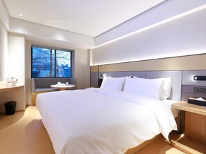 A modern hotel room with a large bed, bedside tables, a small round table, and a window with a view of buildings. - Ji Hotel (Shanghai)