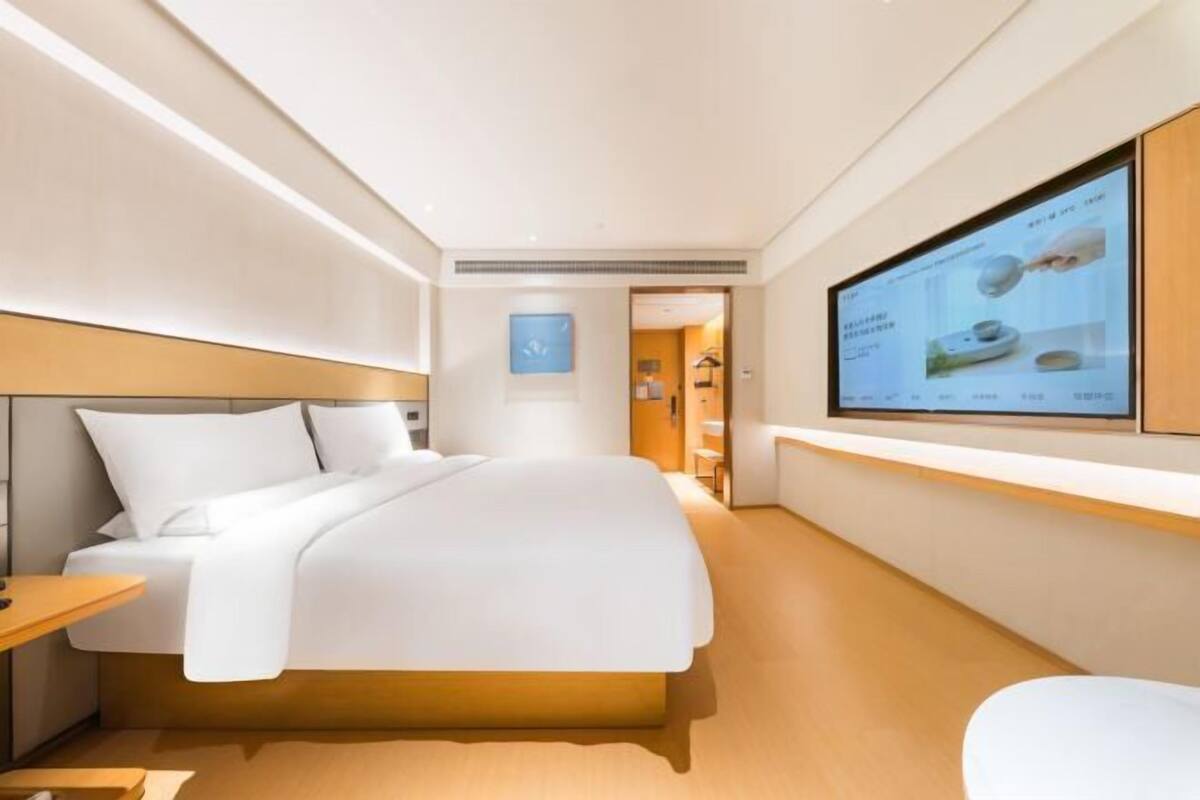 A modern hotel room with a bed, bedside table, and a TV mounted on the wall.