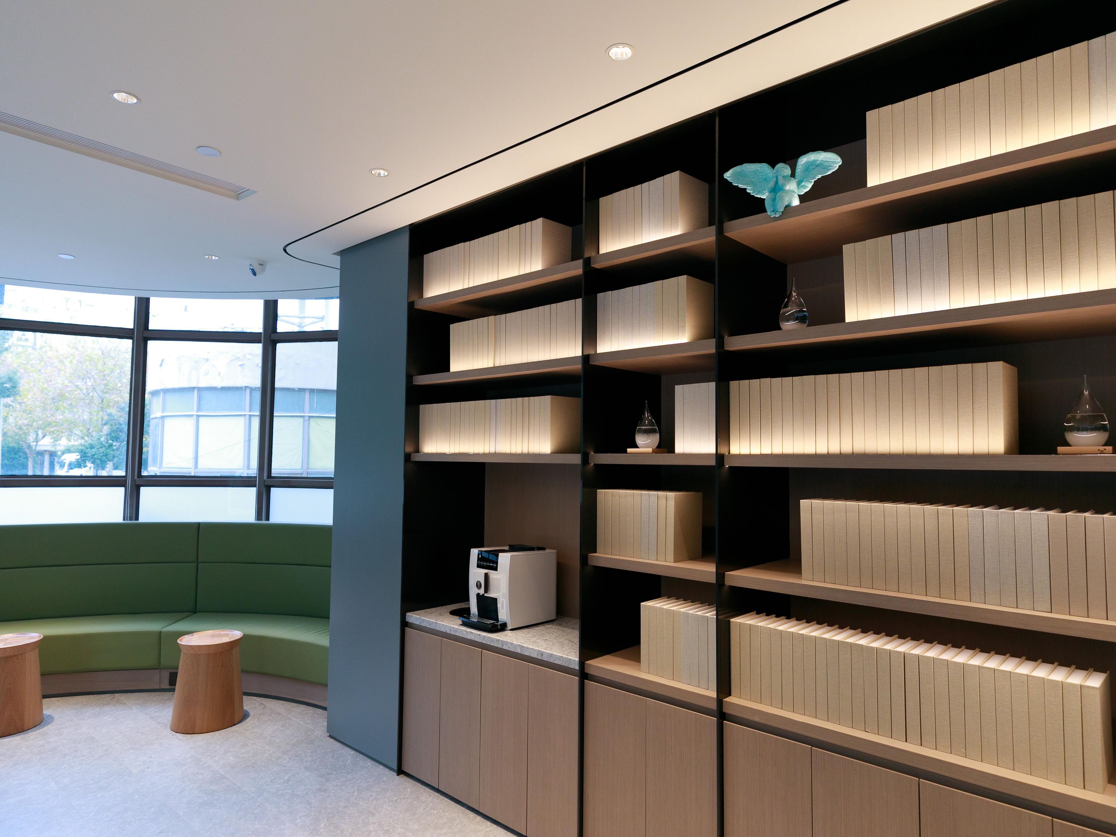 Um interior moderno com área de estar verde, estantes embutidas com objetos decorativos e uma máquina de café.