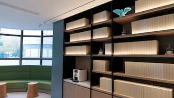 Um interior moderno com área de estar verde, estantes embutidas com objetos decorativos e uma máquina de café.