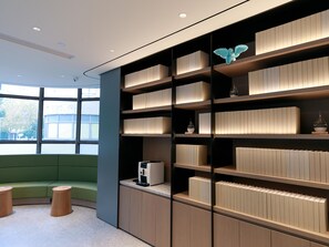 Un intérieur moderne avec un espace détente aux couleurs vertes, des étagères intégrées ornées d’objets décoratifs et une machine à café.