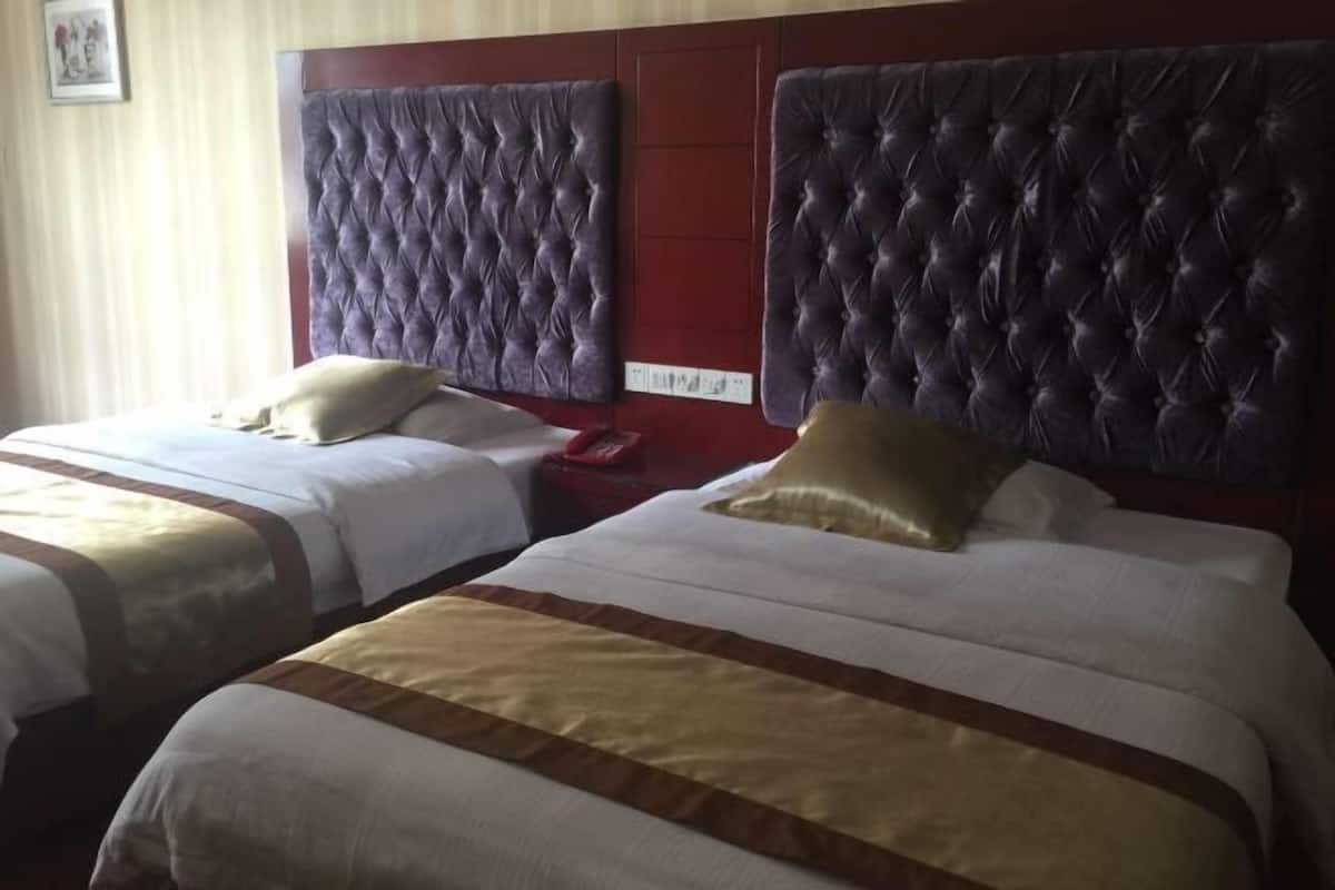 A hotel room with two beds, each with a tufted headboard and a striped bedspread.
